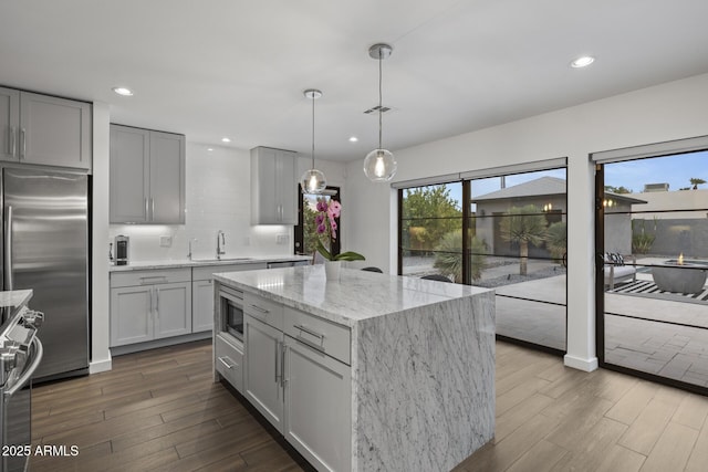 kitchen featuring gray cabinets, built in appliances, light stone counters, a kitchen island, and decorative light fixtures