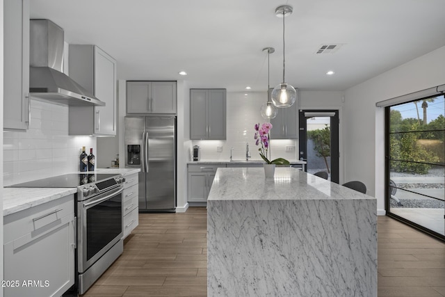 kitchen featuring appliances with stainless steel finishes, light stone counters, a kitchen island, dark hardwood / wood-style flooring, and wall chimney exhaust hood