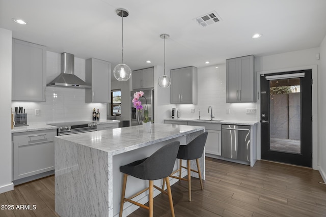 kitchen featuring a kitchen island, appliances with stainless steel finishes, sink, gray cabinetry, and wall chimney exhaust hood