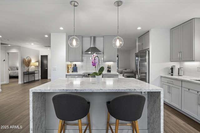 kitchen with light stone counters, stainless steel fridge with ice dispenser, a kitchen island, and wall chimney range hood