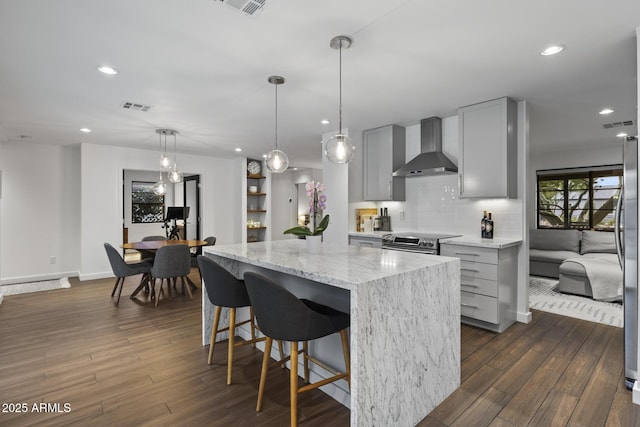 kitchen featuring appliances with stainless steel finishes, dark hardwood / wood-style flooring, gray cabinets, a kitchen island, and wall chimney range hood