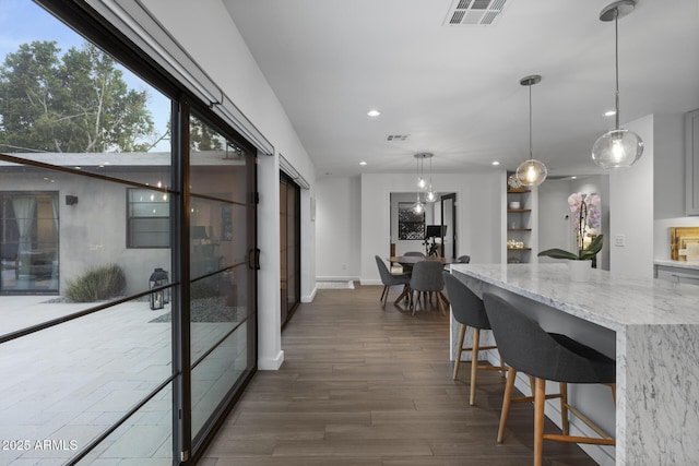 kitchen featuring light stone counters, hanging light fixtures, a breakfast bar area, and dark hardwood / wood-style floors