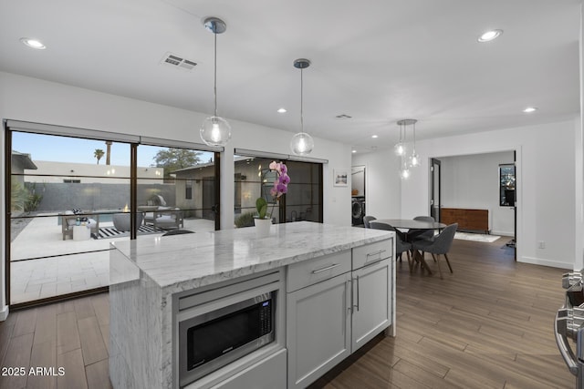 kitchen with light stone counters, hardwood / wood-style floors, pendant lighting, and a center island