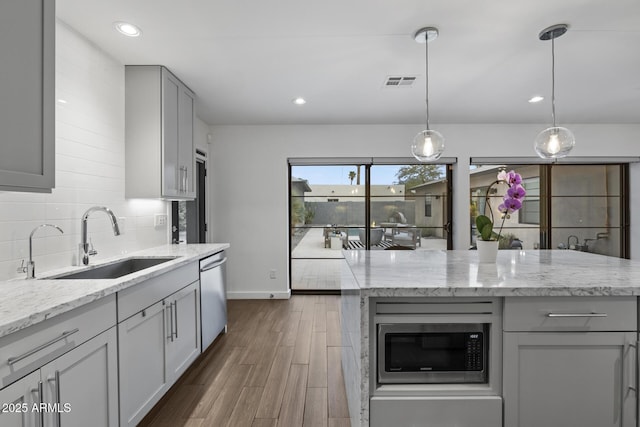 kitchen featuring sink, gray cabinetry, backsplash, stainless steel appliances, and light stone countertops