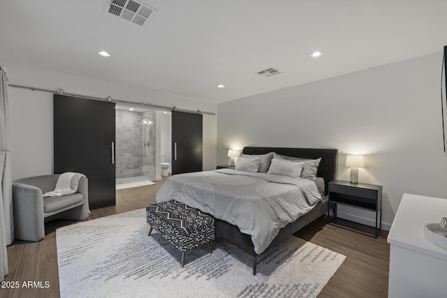 bedroom with ensuite bathroom, a barn door, and dark hardwood / wood-style flooring