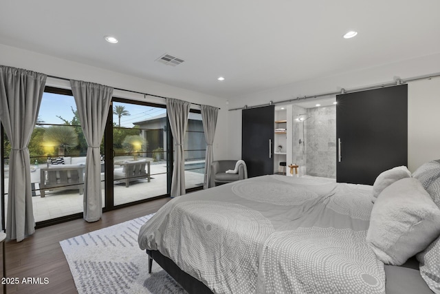 bedroom with a barn door, dark wood-type flooring, and access to outside