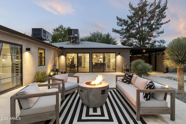 patio terrace at dusk featuring central AC unit and an outdoor living space with a fire pit