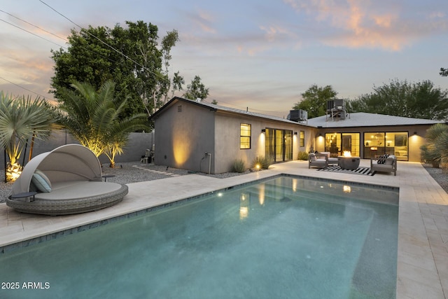 pool at dusk featuring an outdoor living space, a patio area, and central air condition unit