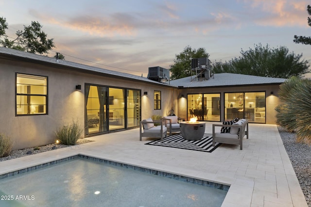 back house at dusk with an outdoor living space with a fire pit, central AC unit, and a patio area