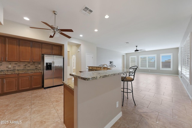 kitchen featuring backsplash, stainless steel fridge, a kitchen breakfast bar, light tile patterned floors, and light stone counters