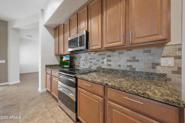 kitchen with tasteful backsplash, light tile patterned flooring, appliances with stainless steel finishes, and dark stone counters