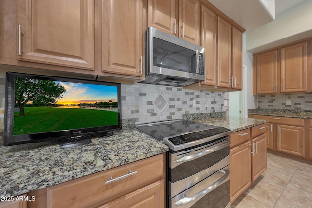 kitchen featuring light stone countertops, appliances with stainless steel finishes, light tile patterned floors, and decorative backsplash