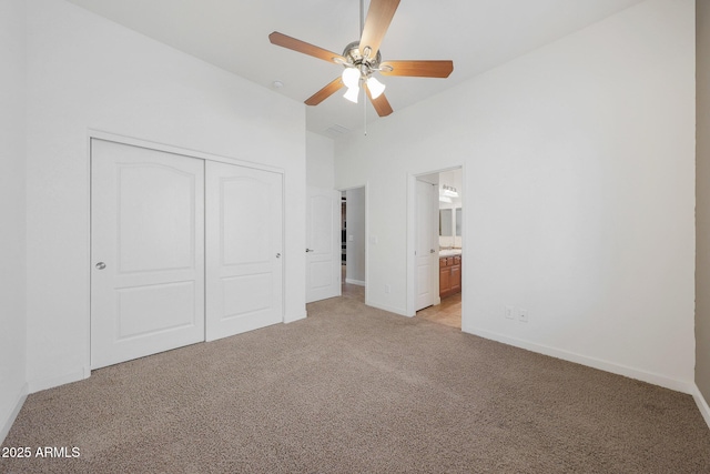 unfurnished bedroom with a towering ceiling, ceiling fan, light carpet, ensuite bath, and a closet