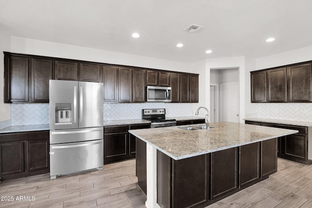 kitchen with sink, dark brown cabinets, stainless steel appliances, and an island with sink