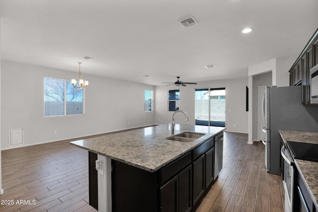 kitchen with pendant lighting, sink, stainless steel appliances, light stone countertops, and a center island with sink