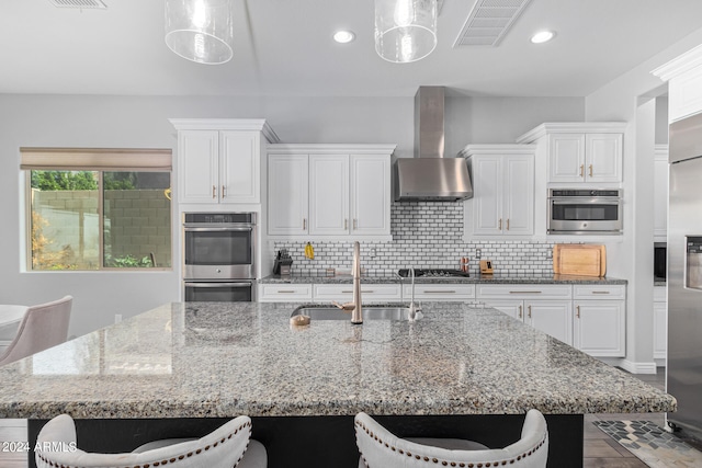 kitchen featuring a kitchen island with sink, pendant lighting, sink, stainless steel appliances, and white cabinetry