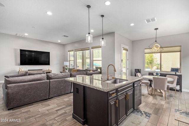 kitchen featuring hanging light fixtures, sink, light stone countertops, and light hardwood / wood-style flooring