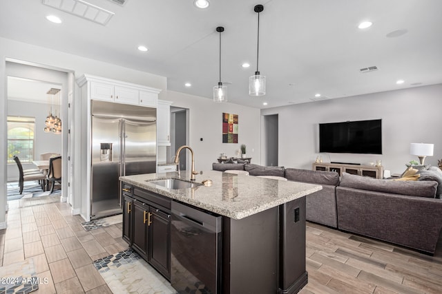 kitchen featuring white cabinetry, decorative light fixtures, appliances with stainless steel finishes, sink, and an island with sink