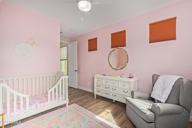 bedroom featuring dark hardwood / wood-style flooring, ceiling fan, and a crib