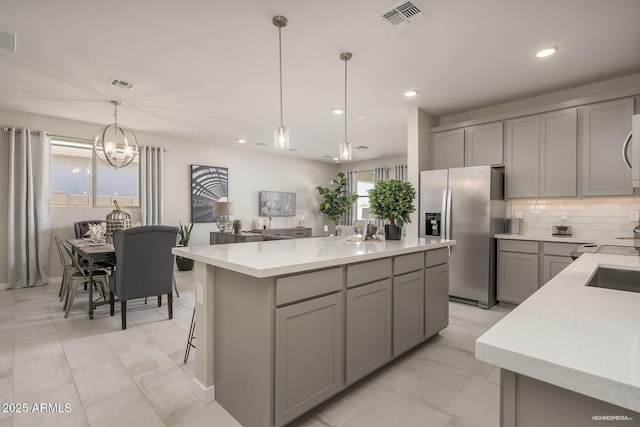 kitchen with decorative light fixtures, gray cabinets, a kitchen island, a notable chandelier, and appliances with stainless steel finishes