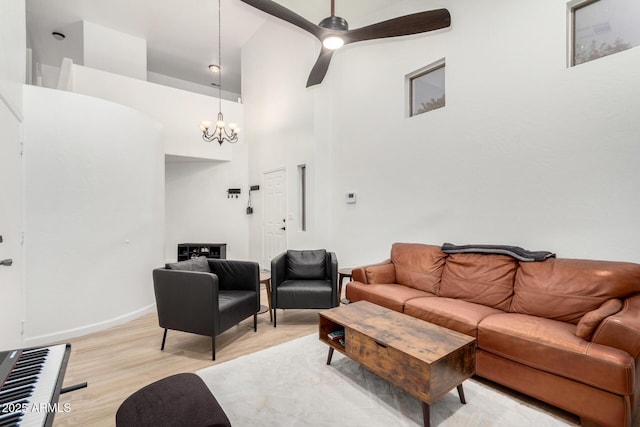 living room with ceiling fan with notable chandelier, light hardwood / wood-style floors, and a high ceiling