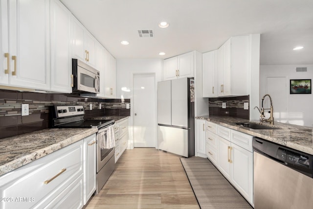 kitchen with sink, appliances with stainless steel finishes, white cabinetry, light stone countertops, and light wood-type flooring