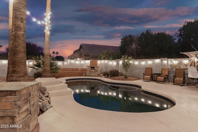 pool at dusk with a fireplace and a patio