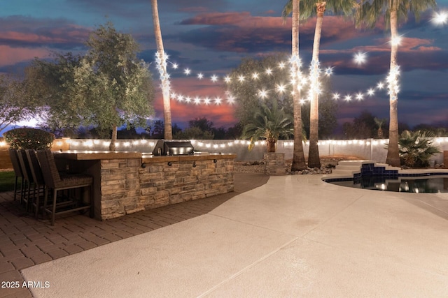 patio terrace at dusk featuring exterior kitchen and an outdoor bar