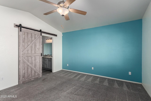 unfurnished bedroom featuring vaulted ceiling, ceiling fan, dark colored carpet, a barn door, and connected bathroom