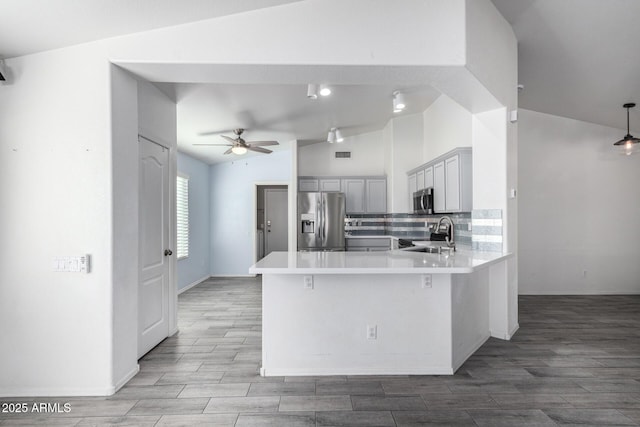 kitchen featuring lofted ceiling, backsplash, appliances with stainless steel finishes, a kitchen bar, and kitchen peninsula