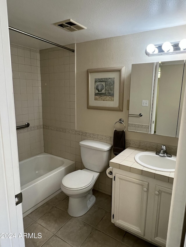 full bathroom featuring tiled shower / bath combo, tile patterned floors, toilet, vanity, and tile walls