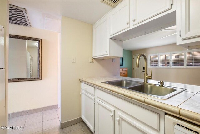 kitchen with white appliances, sink, light tile patterned floors, white cabinets, and tile counters