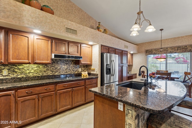 kitchen with black electric stovetop, sink, pendant lighting, a center island with sink, and stainless steel fridge with ice dispenser