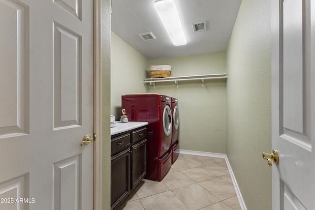 laundry area with washing machine and dryer, light tile patterned flooring, cabinets, and a textured ceiling