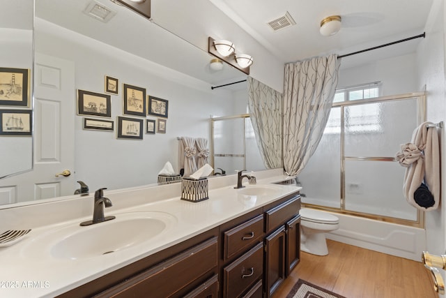 full bathroom with hardwood / wood-style flooring, vanity, toilet, and combined bath / shower with glass door