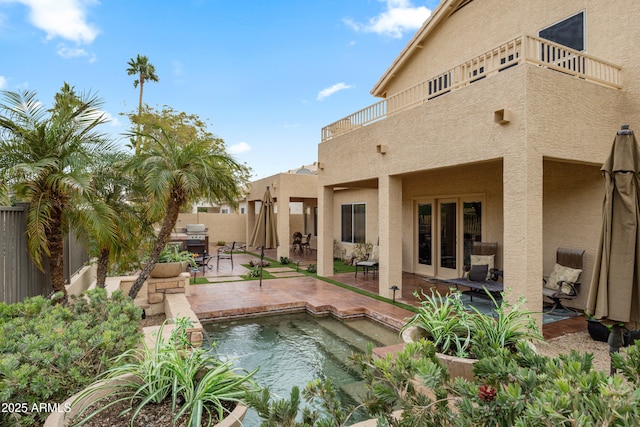 rear view of property featuring a patio area, a balcony, and a fenced in pool