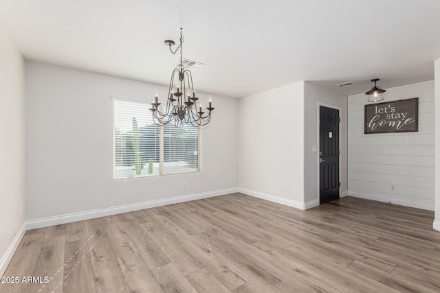 empty room featuring a notable chandelier and light hardwood / wood-style floors