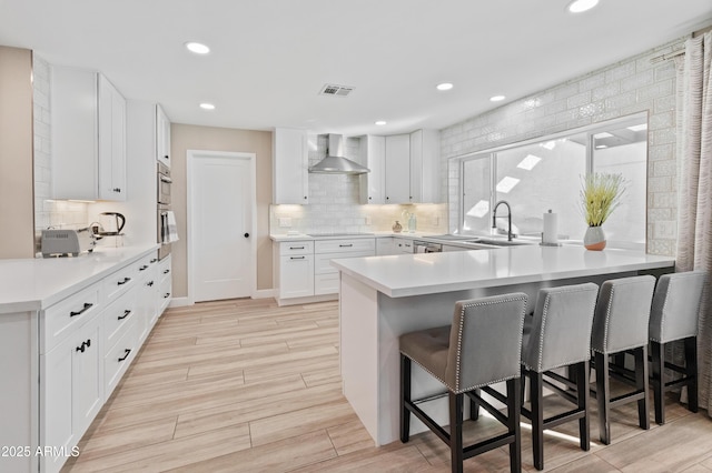 6220 E Paradise Ln, Scottsdale, AZ 85254 - kitchen with a peninsula, wall chimney range hood, a kitchen bar, white cabinets, and backsplash