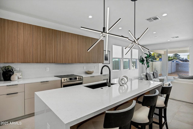 kitchen featuring sink, hanging light fixtures, a kitchen island with sink, a breakfast bar, and stainless steel electric range