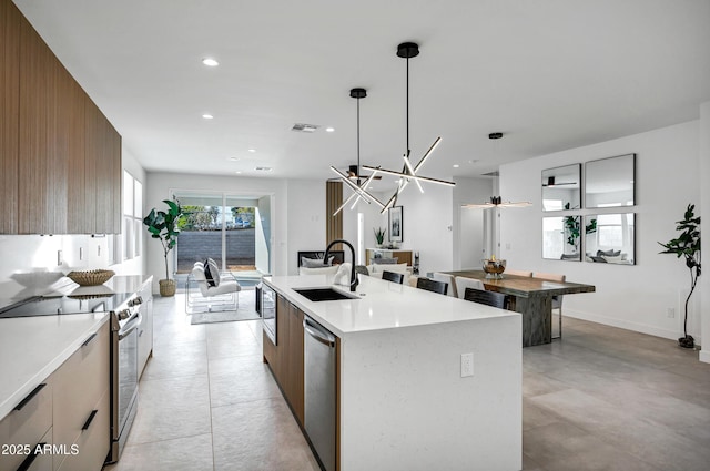 kitchen with sink, wooden walls, hanging light fixtures, an island with sink, and stainless steel appliances