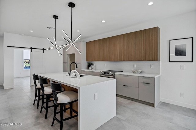 kitchen featuring pendant lighting, an island with sink, sink, stainless steel electric range oven, and a barn door