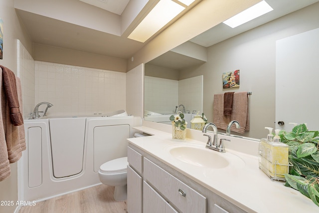 bathroom featuring hardwood / wood-style floors, a skylight, vanity, a tub to relax in, and toilet