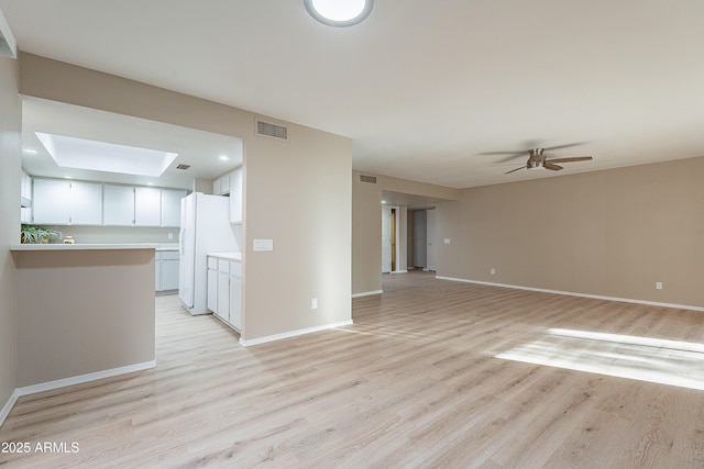 unfurnished living room with ceiling fan, a skylight, and light hardwood / wood-style floors