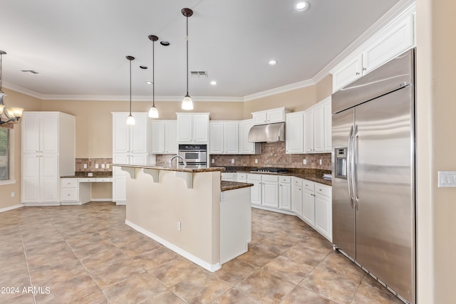 kitchen featuring a breakfast bar area, an island with sink, hanging light fixtures, stainless steel appliances, and white cabinetry