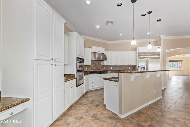 kitchen with appliances with stainless steel finishes, decorative light fixtures, white cabinetry, and dark stone countertops