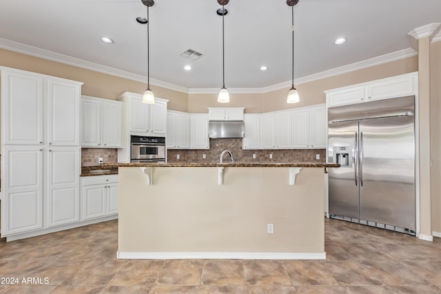 kitchen with white cabinets, appliances with stainless steel finishes, a breakfast bar, a kitchen island with sink, and dark stone counters