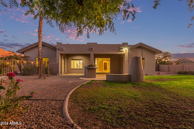 back house at dusk featuring a patio and a lawn