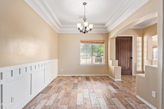 interior space with light hardwood / wood-style floors, a notable chandelier, ornamental molding, and a tray ceiling