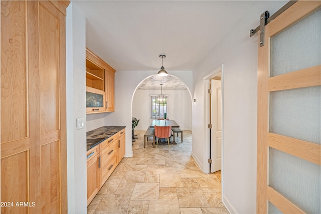 hall with a barn door, arched walkways, stone finish floor, and baseboards