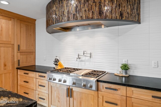 kitchen with dark stone counters, light brown cabinets, custom exhaust hood, stainless steel gas cooktop, and backsplash